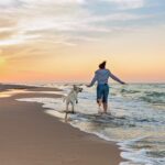 Frau tollt mit ihrem Hund über den Strand